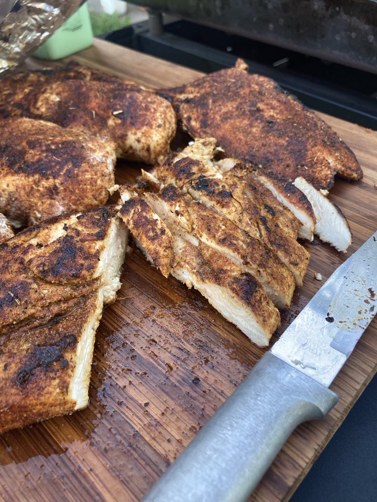 Seasoned chicken sliced on a cutting board with knife next to it