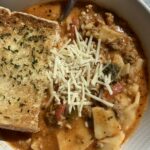 Pasta soup topped with cheese and garlic bread